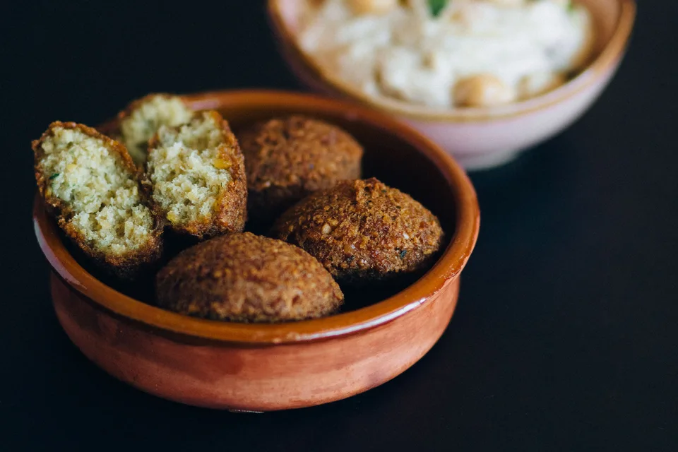 BookNoFees: Primjer fotografije: Falafel kuglice, uključujući jedan presječen komad, u zdjeli s humusom u pozadini