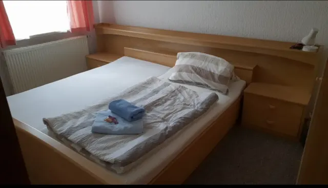 BookNoFees: smještaj za odmor, Schönfeld – Spavaća soba s drvenim okvirom kreveta, složenim ručnicima i prozorom s ružičastim zavjesama
